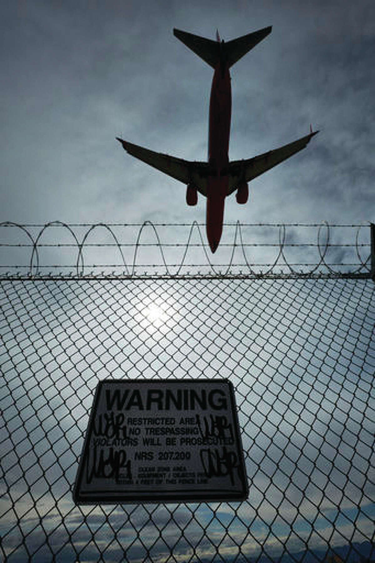 In this May 17, 2016, photo, a sign warns against trespassing as a plane lands at McCarran International Airport in Las Vegas. An Associated Press investigation has documented perimeter breaches at many of the busiest airports in the U.S.