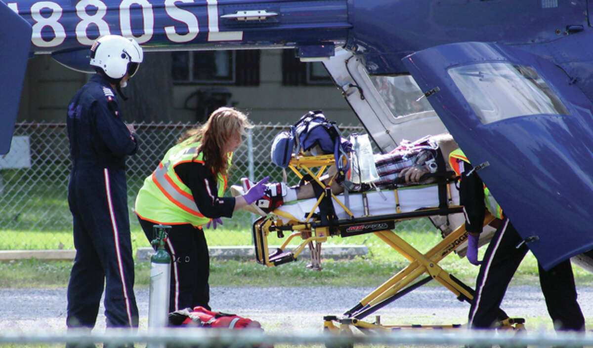 An ARCH Air Medical Services helicopter pilot, left, watches as paramedics load a man into the helicopter after he was shot in the chest Tuesday afternoon. The helicopter landed at South Roxana Dads Club Park, a few blocks away from where police officers had set up a crime scene on Smith Avenue.