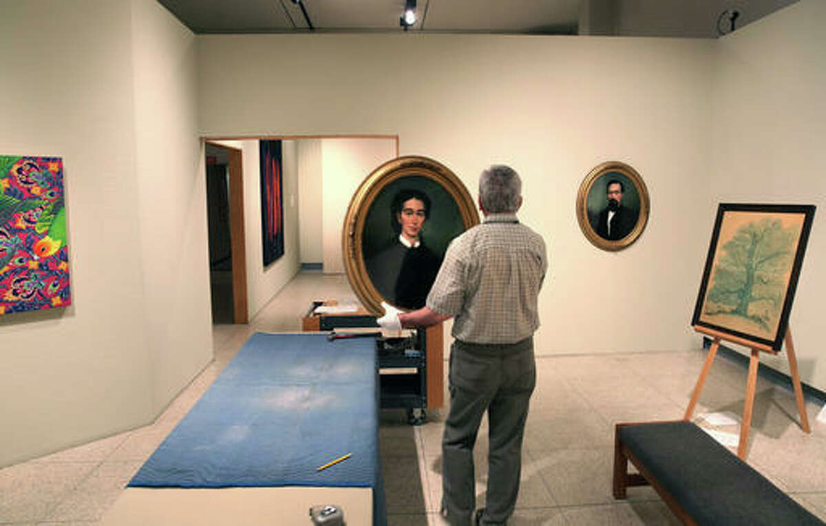 In this June 2, 2016 photo, Illinois State Museum employee Phil Kennedy prepares to hang a reverse painting on glass portrait of Prudence Capps Beidler from 1867 in the museum in Springfield, Ill. The museum could reopen soon, after being closed since October due to the state budget impasse. The state's Department of Natural Resources said the museum could reopen July 2, following approval of an admission charge to the main museum campus. (David Spencer/The State Journal-Register via AP)
