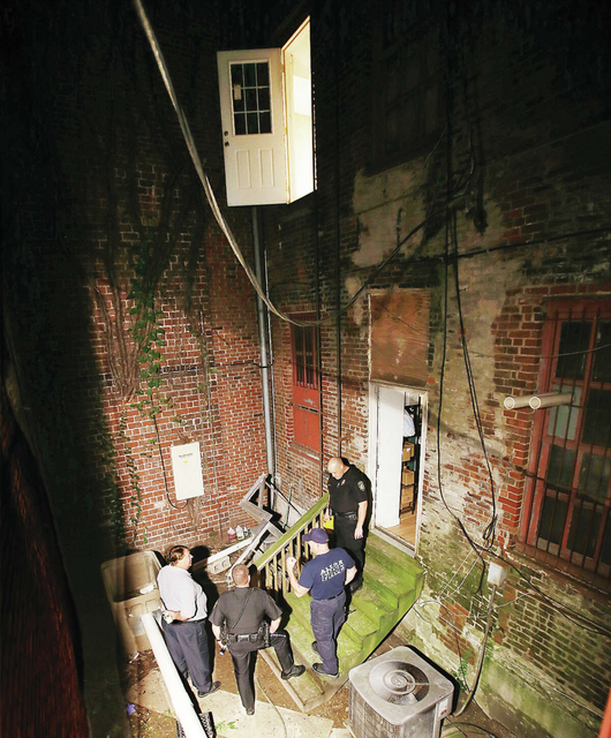 Alton police and fire department officials gather behind the Olive Oil Marketplace at 108 W. Third St. in Alton where a metal fire escape platform, with three people on it, collapsed after coming loose from the brick wall, above, late Sunday night injuring the three people. Two were transported to OSF Saint Anthony’s Medical Center in Alton, where one victim was flown by helicopter ambulance to a St. Louis trauma center. Russ Smith, who owns other buildings in Downtown Alton also owns the building where the accident occurred.