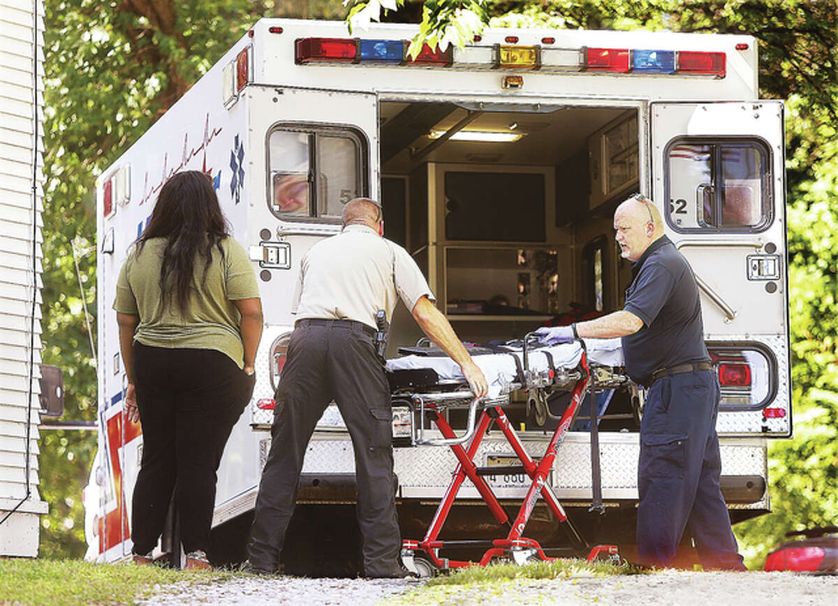 A woman watches as a Madison County deputy coroner, center, and a LifeStar Ambulance paramedic unload a stretcher to pick up an apparent tandem heroin overdose in a triplex at 1500 Sparks St. in Alton Thursday. Police arrived to find two people deceased in one of the apartments. Alton Police Chief Jake Simmons called it part of the national epidemic of heroin deaths.