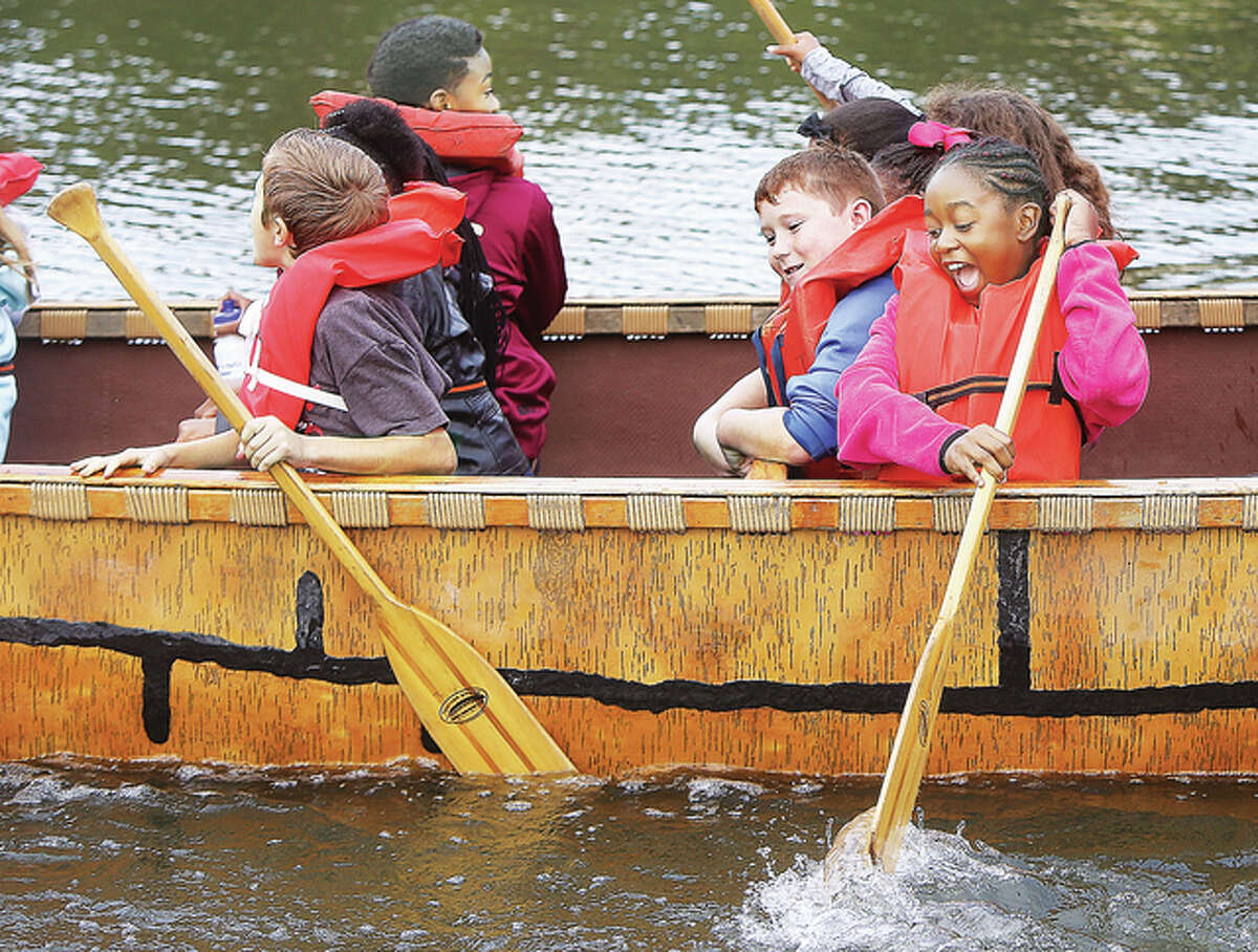 Fifth grade students from North Elementary School in Alton, including an excited girl trying to paddle, react as the replica voyageur canoe they were in rocks back and forth on the water at the water festival Friday. The voyageur canoe was popular for many decades prior to 1840.