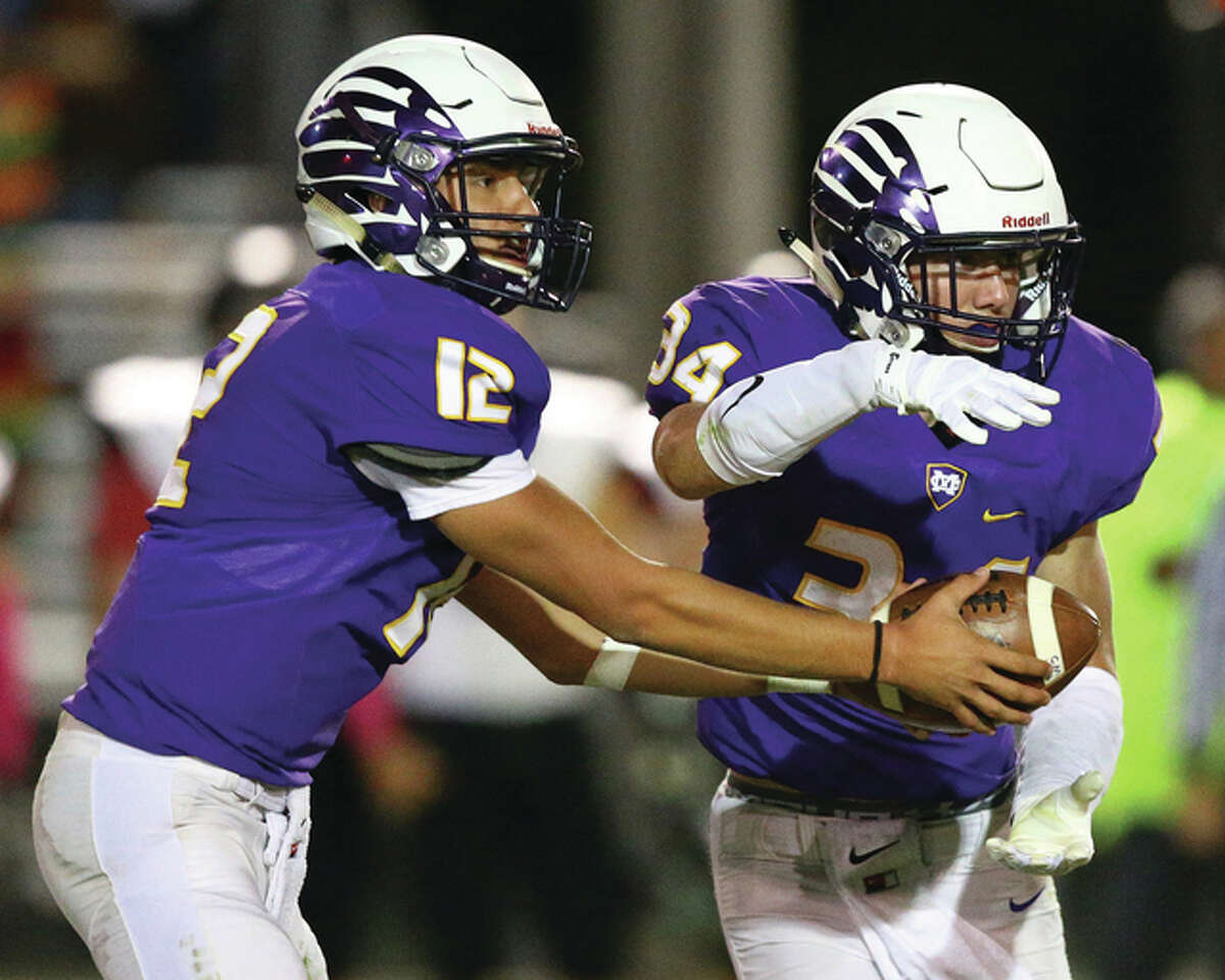 CM quarterback Adam Hill (left) hands the ball off to running back John Whitworth during the second half of Friday night’s Mississippi Valley Conference game against the Highland Bulldogs in Bethalto.