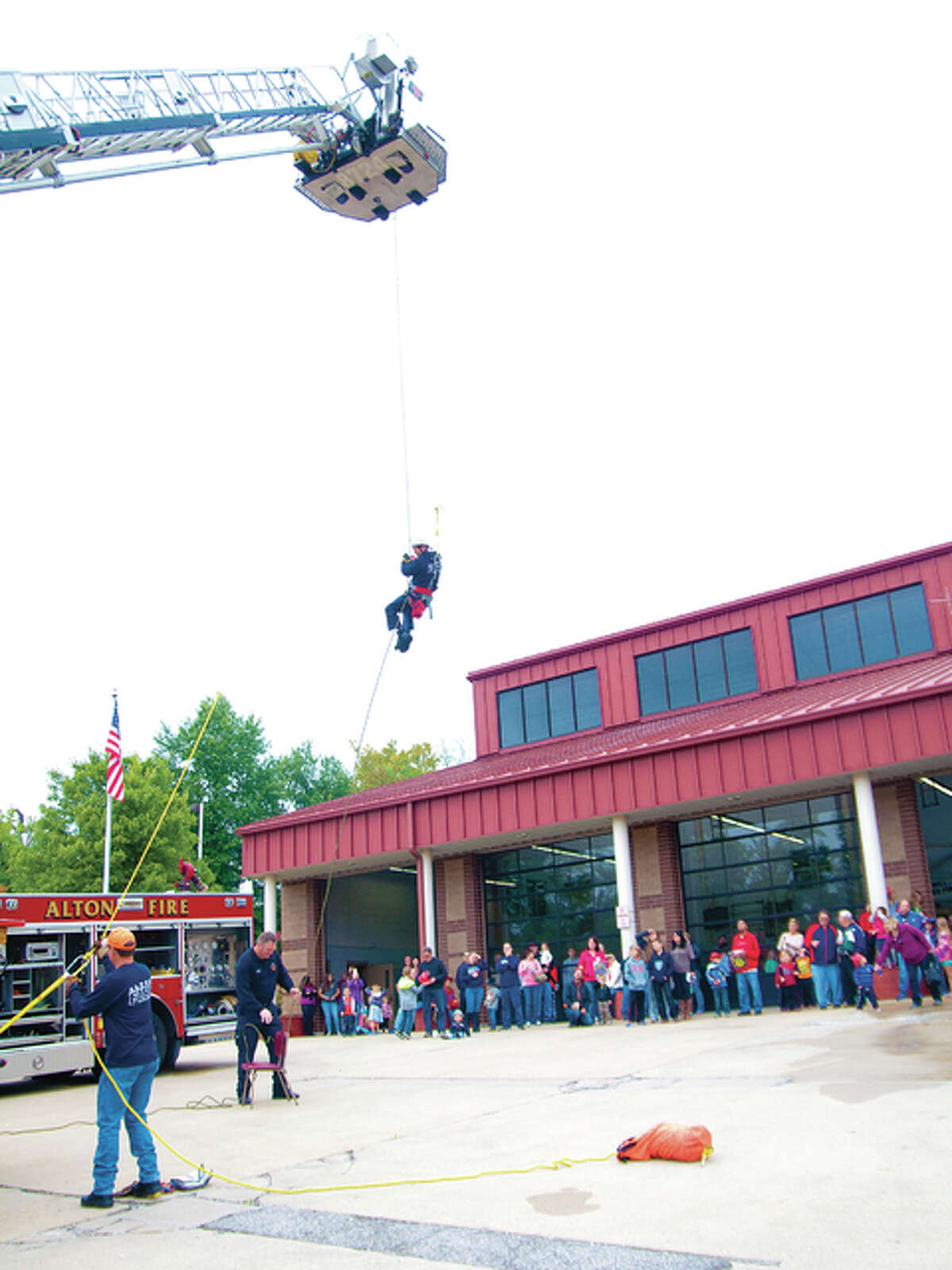 A crowd of people watches Cliff Holshouser of the Alton Fire Departments Tactical Rescue Unit repel down from 75 feet in the air to simulate a rescue on difficult terrain.
