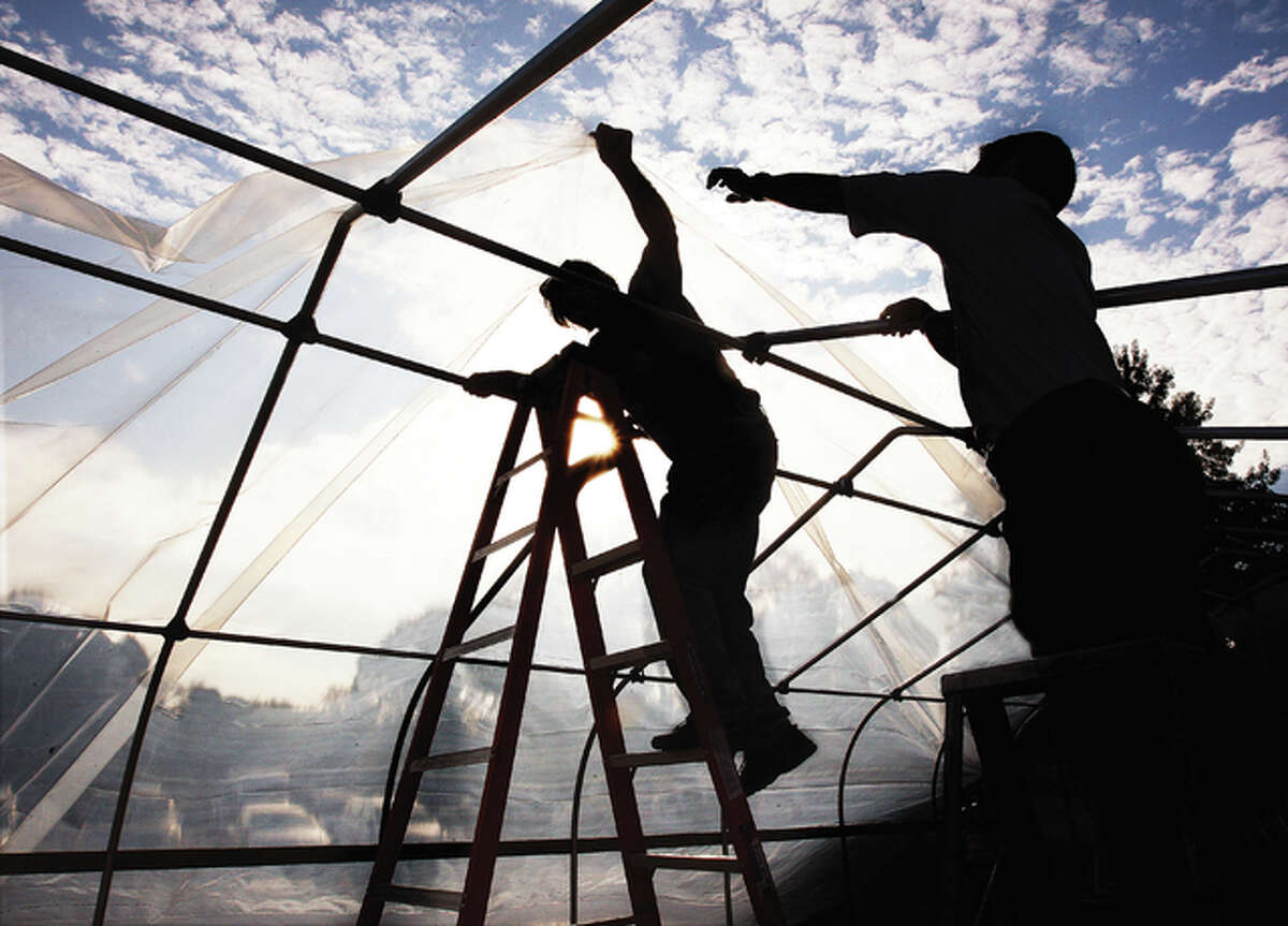 Workers were silhouetted recently as they stretched a thick plastic covering over the framework of a new greenhouse at Senior Services Plus located directly behind the senior center in Alton.