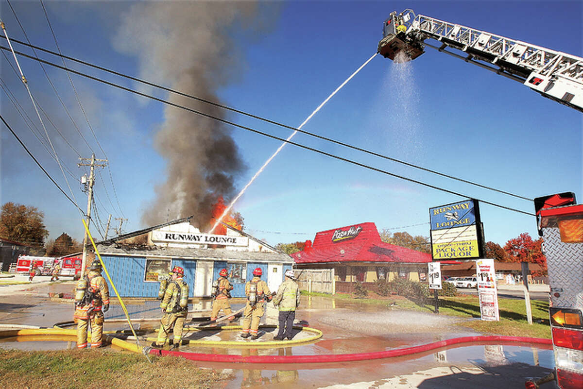 An aerial ladder truck from the Alton Fire Department dumps water on the business as flames break through the roof. Firefighters attempted to fight the fire from the front door but the blaze had spread too far, too fast. The tower truck was able to save the rear portion of the structure.