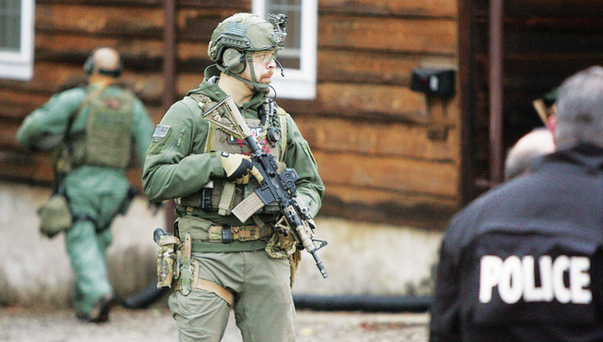 A heavily armed tactical team member keeps a sharp eye on the perimeter of the duplex as the prisoners are loaded for transport to jail. Detectives remained on the scene for at least an hour after the raid.