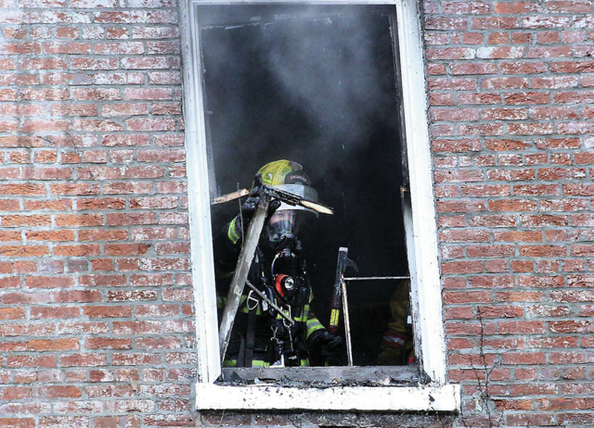 An Alton firefighter clears the window out of a historic home on Mills Avenue in Alton Saturday morning. It’s believed an unwatched lit cigarette caused the blaze that destroyed one apartment and heavily damaged two others.