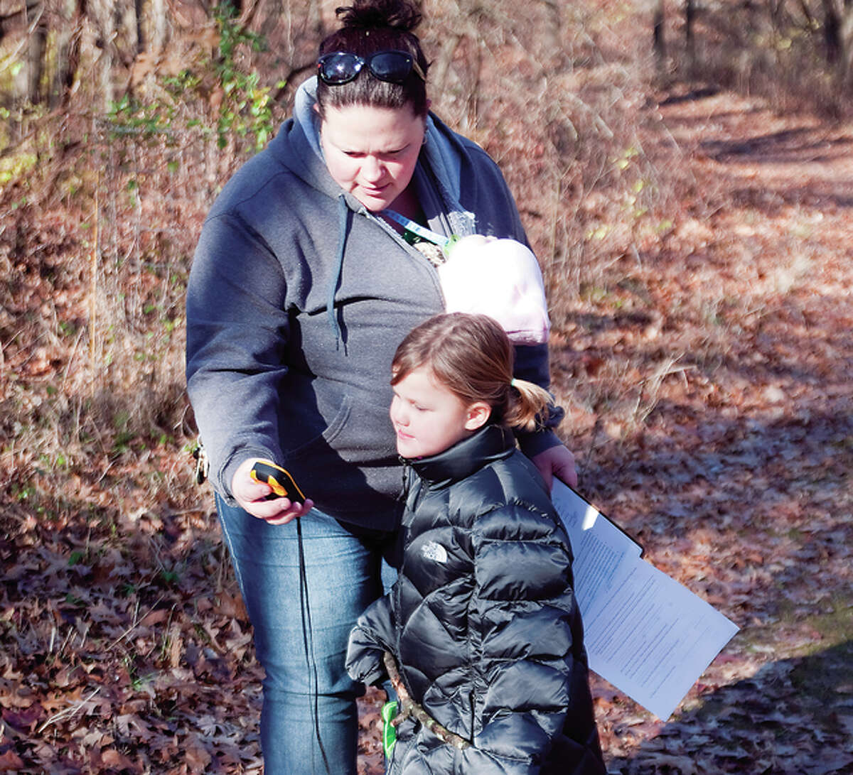 Five-year-old Caitlyn Stafford looks at the GPS locator that her mom Kelly Stafford holds in her hand while 3-month-old Maxine is bundled inside of Stafford’s coat. The Staffords were trying to locate one of the eight candy canes that were mapped out somewhere on property of The Nature Institute.