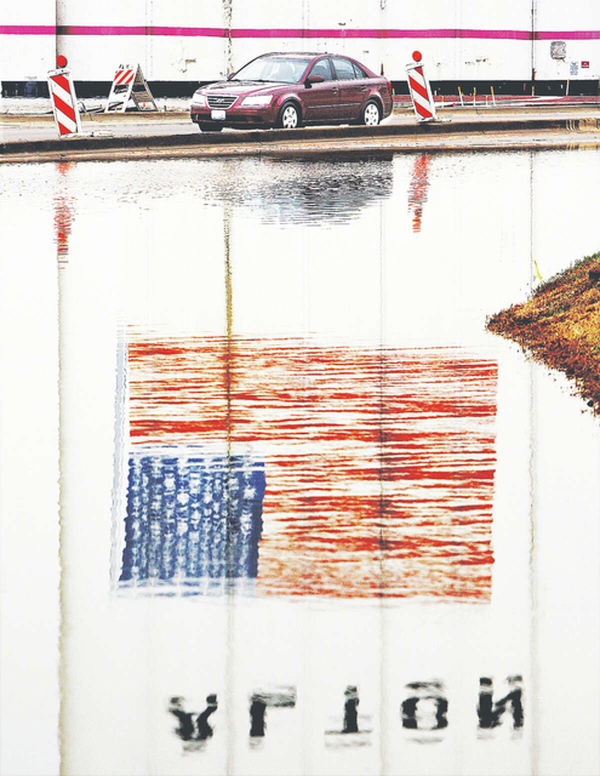A motorist heads east on Landmarks Boulevard in downtown Alton in late December, past floodwaters covering the westbound lanes that were reflecting the large American flag painted on the Ardent Mills silos. The red line above the car is the flood level mark from the Great Flood of 1993.
