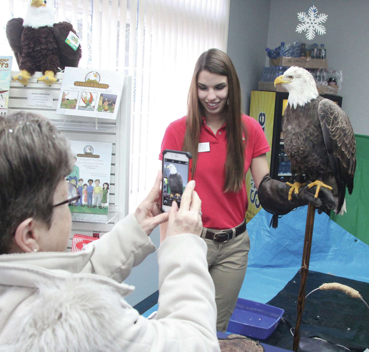 Godfrey resident Nancey Blackburn takes a photograph of Liberty, a 23-year-old bald eagle, held by naturalist Paige Davis, with the World Bird Sanctuary, during the Alton Eagle Meet and Greet at the Greater Alton Regional Convention and Visitors Bureau Saturday morning.