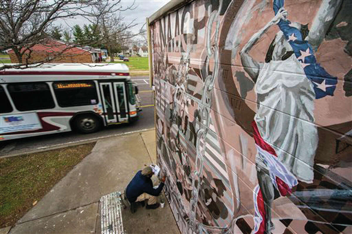 In this Dec. 11, 2015 photo, artist R. Rashad Reed works on completing a mural on the outside entrance of the Peoria NAACP office in Peoria, Illinois, to commemorate the 100th year of the Peoria NAACP.