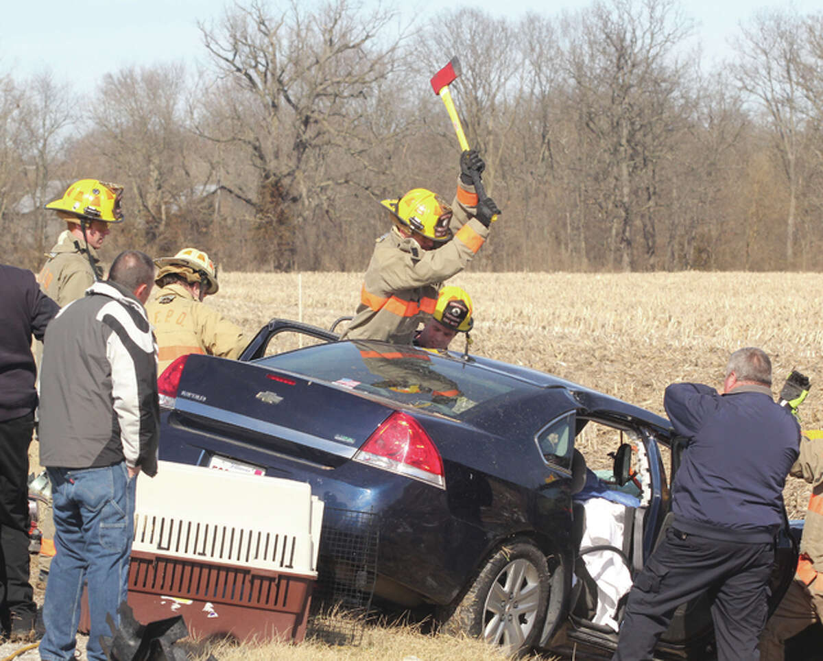 A firefighter uses an ax as emergency responders get ready to peel the roof off of a car to extricate two people after a head-on collision on Fosterburg Road early Saturday afternoon. At least three people were injured, and several were airlifted to local hospitals.