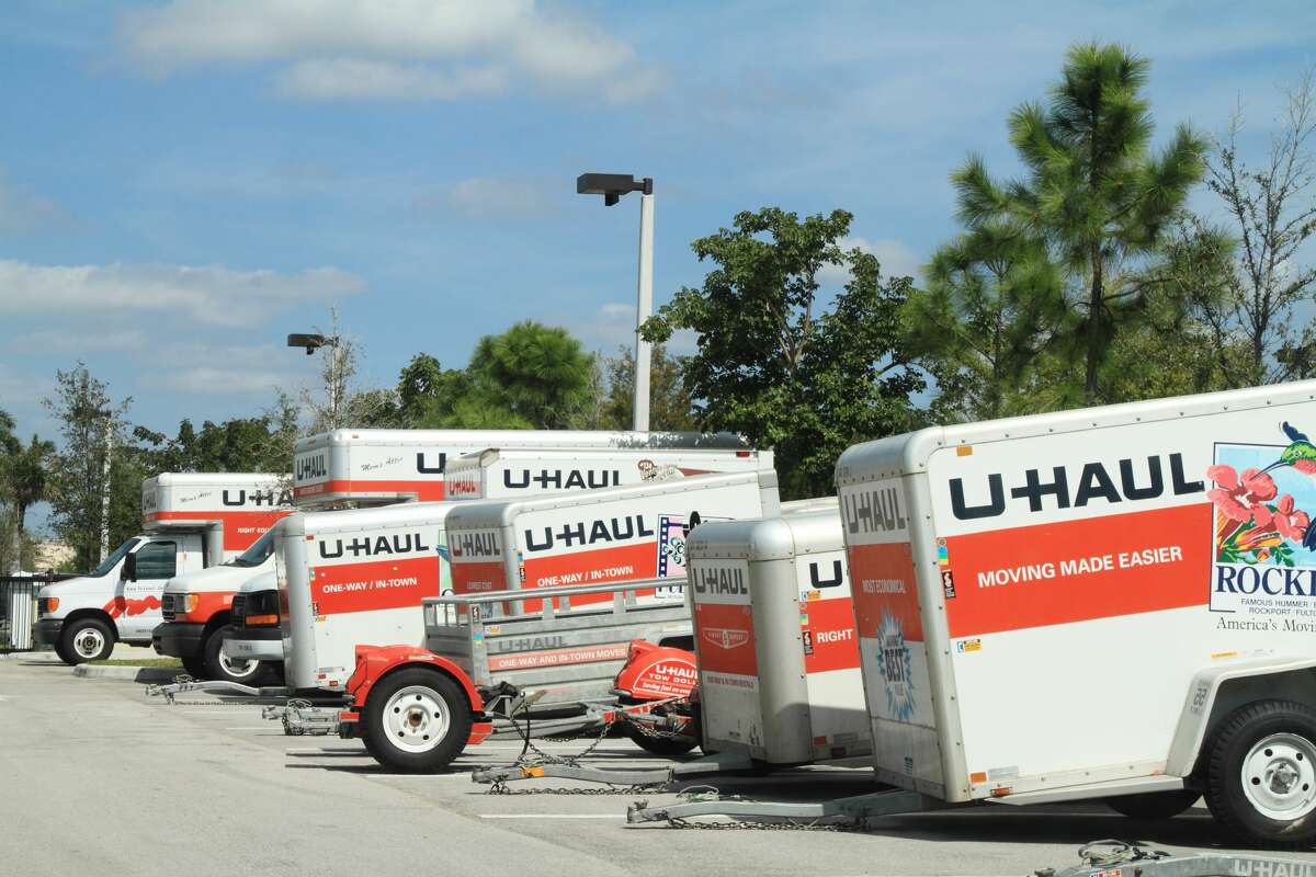A row of U-Haul trucks and trailers are parked in a storage lot.