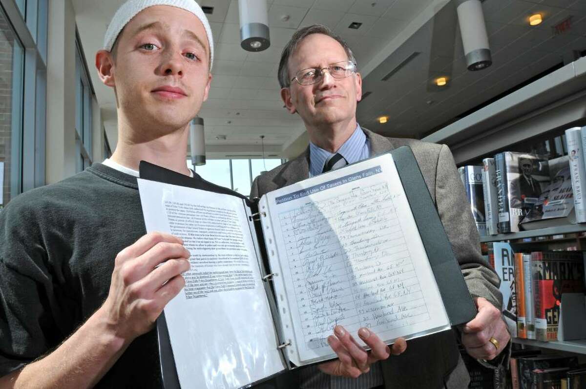 Christopher Schmidt, left, and teacher Peter Duveen hold a petition, signed by hundreds, to get rid of police Tasers in Glens Falls. (Lori Van Buren / Times Union)