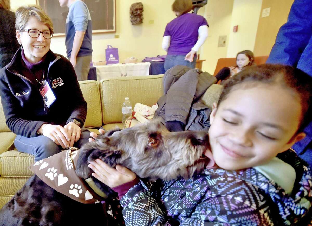 Leila Martinez, 8, of New Haven, right, gets a kiss from certified therapy dog Sophia, a rescued mixed-breed, on Saturday with her handler Roben River, of Woodbridge, representing dog training facility Paw’s N’ Effect of Hamden .