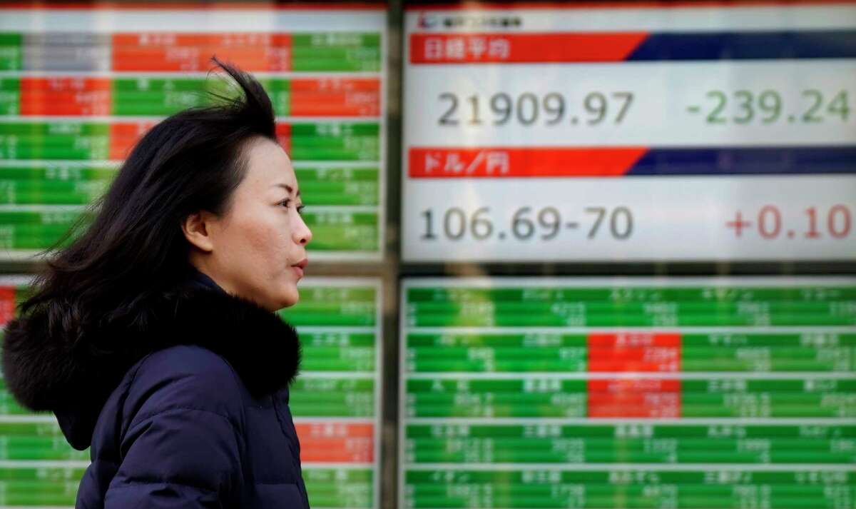 A woman walks past an electronic stock indicator of a securities firm in Tokyo, Tuesday, Feb. 20, 2018. Asian shares were mostly lower Tuesday after a U.S. holiday and attention turned to the U.S. Federal Reserve. (AP Photo/Shizuo Kambayashi)