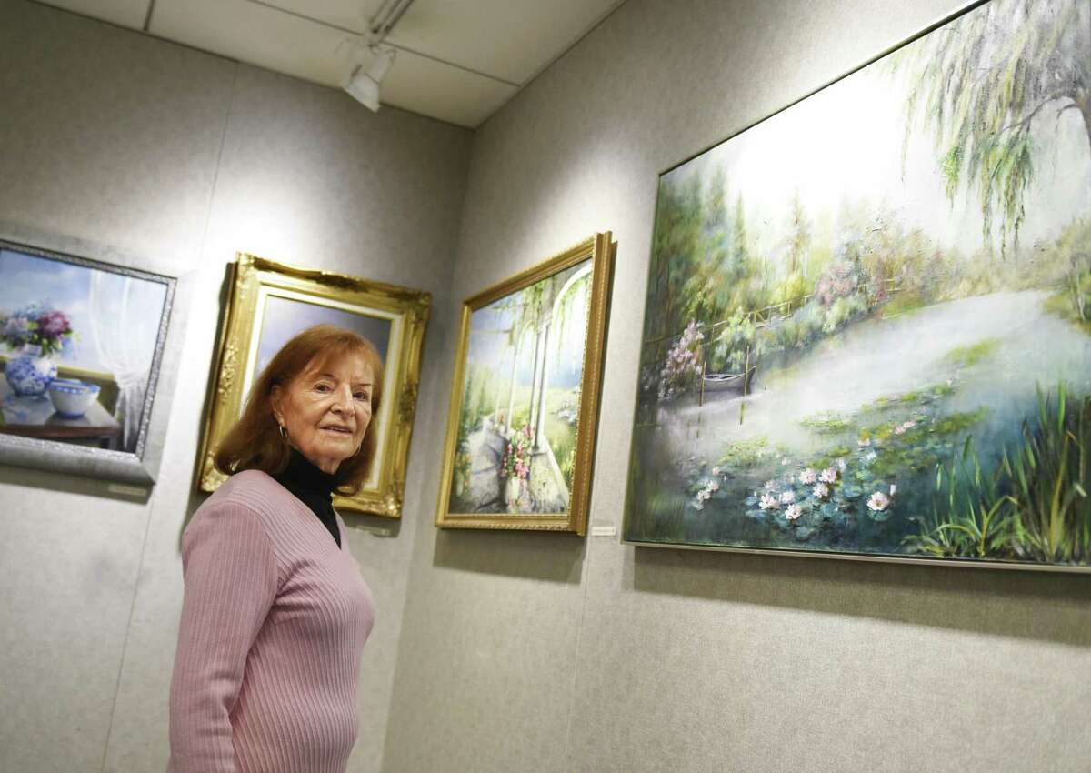Greenwich artist Lucie Anderes poses by her work, including the piece "Luminous Fibration," right, on display at the YWCA in Greenwich, Conn. Thursday, Feb. 15, 2018. Anderes's oil paintings feature soft-colored impressionistic scenes and still lifes ranging from her backyard, to Maine, to Morocco.