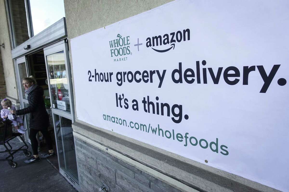 A sign promoting the Amazon Prime Now delivery service is displayed outside a Whole Foods store, Thursday, Feb. 8, 2018, in Cincinnati. Amazon, which owns Whole Foods, plans to roll out two-hour delivery at the organic grocer this year to those who pay for Amazon's $99-a-year Prime membership. Amazon.com Inc. said deliveries started Thursday in Austin, Texas; Cincinnati; Dallas; and Virginia Beach, Va. (AP Photo/John Minchillo)