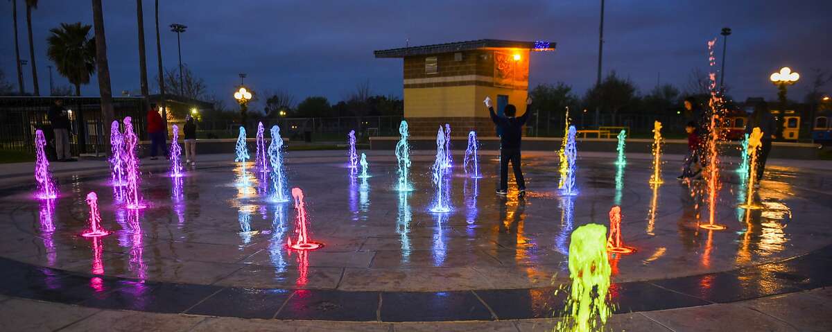 Children dodge LED illuminated jets of water spurting from the ground after ribbon cutting ceremony for the Slaughter Park Splash Park on Thursday, Feb. 22, 2018, at Slaughter Park.