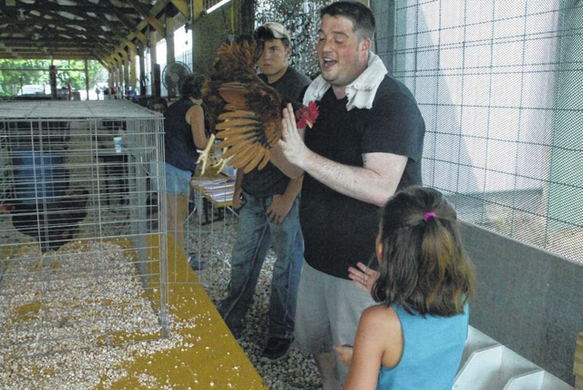 Scott County 4-H and Junior Fair poultry judge Bobby VanBebber of Murrayville talks with Lilly Blakey, 8, (foreground) and her Rhode Island Red hen, Pooper, who won first place Tuesday in the American pullet division at the fair. It was Lilly’s first entry in the fair. Lilly is the daughter of Molly and Travis Blakey of Winchester.