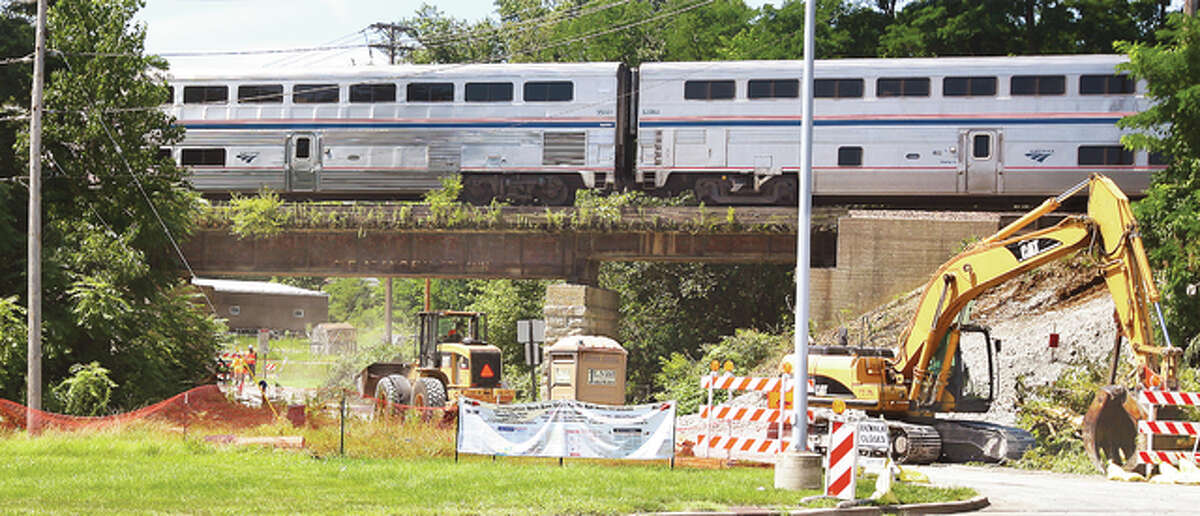 An Amtrak train speeds over the wooden tied railroad viaduct over Seminary Street in Alton just north of Claire Street as workers in heavy equipment clear trees and brush to make way for a new viaduct. The railroad ties on the old viaduct are rotting and in poor condition. The new viaduct will be supported by pillars farther apart making the roadway wider and safer underneath.