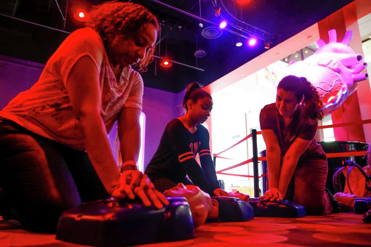 U﻿niversity of Texas medical student Regan Puckett, right, teaches Stacy Gant﻿ and her daughter, Kennedy﻿, 9, the two steps that can help save a life - calling 911 and compression-only CPR﻿ - at The Health Museum in Houston on Sunday.﻿