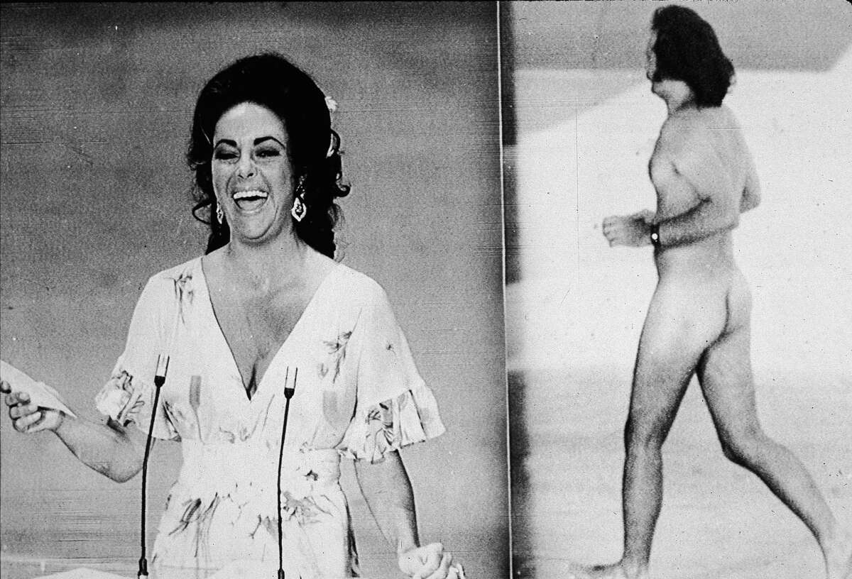 Elizabeth Taylor laughs at being upstaged by streaker Robert Opal before presenting the Oscar for Best Picture at the 46th annual Academy Awards ceremony on April 2, 1974. At right, Opal darts across the stage naked just as David Niven was introducing Taylor. Scroll through to see iconic Oscars images through the years.