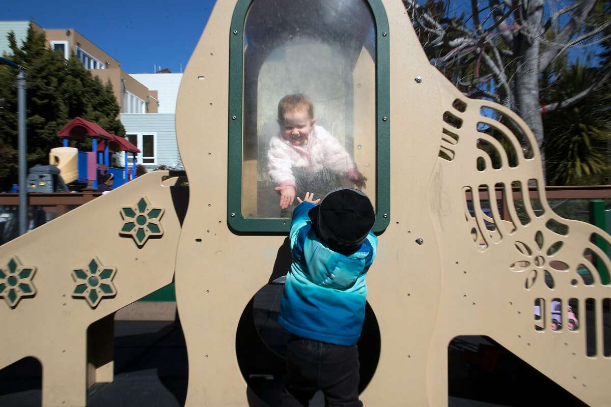 Simone Alley, 22-months reaches down to Ezekiel Gibson, 20-months at the Holy Family Day Home on Tuesday, Feb. 27, 2018 in San Francisco, CA. If the child care ballot measure passes, it would help families pay tuition at centers like this one.