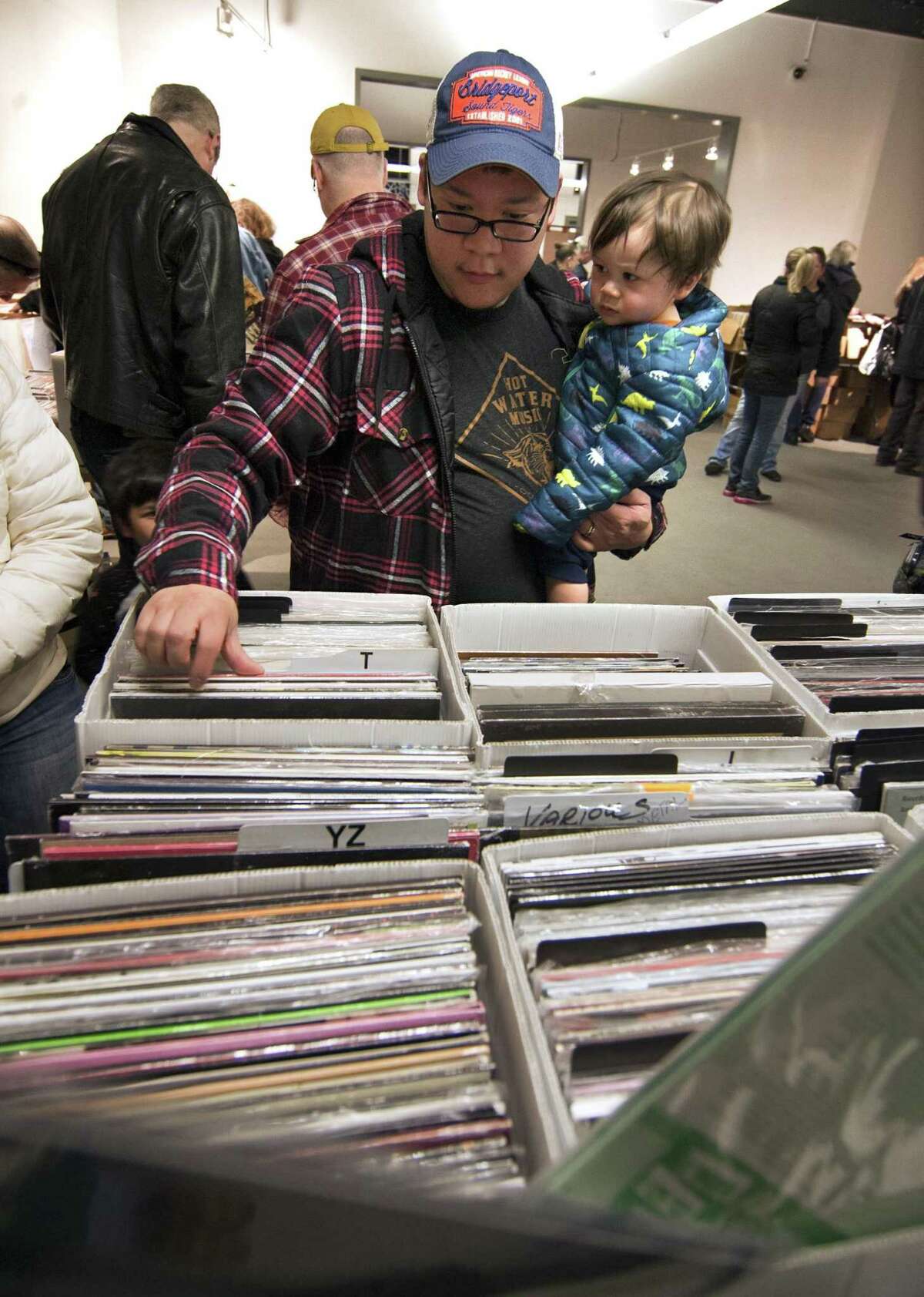 Doug Eng, of Trumbull, looks through boxes of records as he holds his son Arlan, 1, during WPKN's MUSIC MASH Record Fair 2018 at Read's Artspace building on Broad Street in Bridgeport, Conn., on Saturday, Mar. 3, 2018. MUSIC MASH 2018 featured 50+ vendors from all over New England selling vinyl LP's, 45's, CD's and music collectibles.