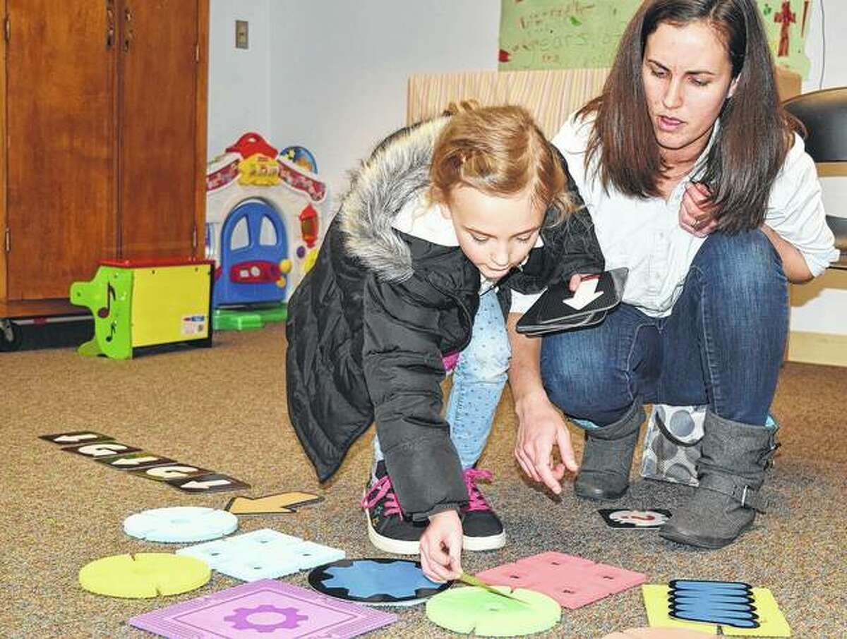 Eleanor Mack, 5, the daughter of Brette and Keenan Mack of Jacksonville, plays “Let’s Go Code” on Monday at the Jacksonville Public Library with the help of her mother. The game asks children to create a path with obstacles to a robot and then has them create a code, or set of directions, to reach the robot, including moves such as going straight, turning, picking up an item and rocketing over a spot.