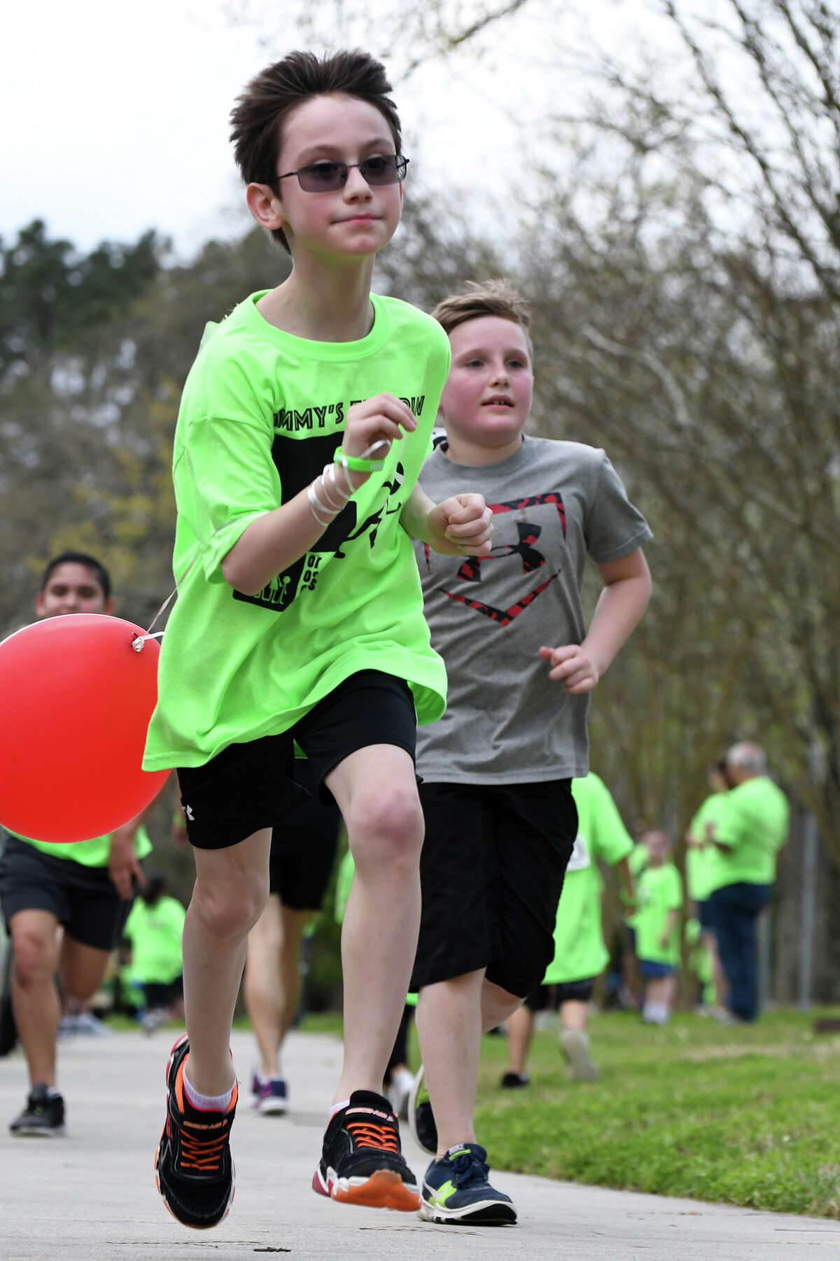 Timmy Schultz, 8, left (holding balloon), runs ahead of Ben Branch 3rd grade classmate Ethan Simms, 8 1/2, right, as they push to the finsih line during the annual "Timmy's Adoption Fun Run" at Kingwood United Methodist Church on March 4, 2018. (Photo by Jerry Baker/Freelance)