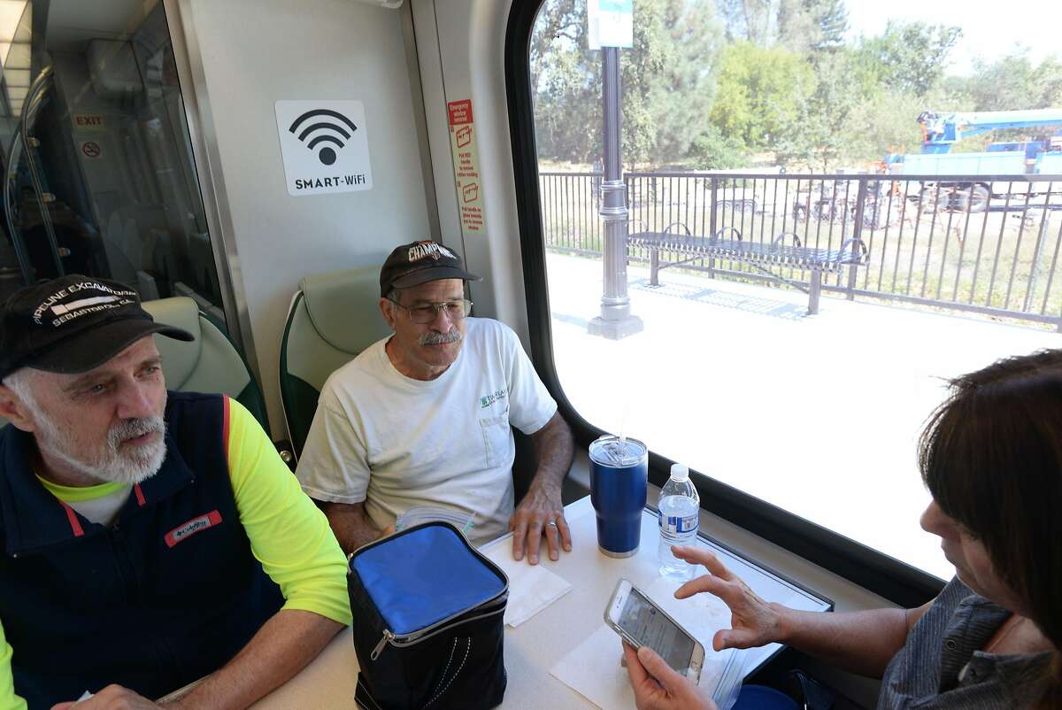 Passenger Laura Babbini, right, of Windsor, California logs on to SMART train WIFI with her smart phone before leaving to San Rafael with Wayne Britton, left, of North Carolina and John Wimmer of Santa Rosa during the first day of SMART train service departing from the Sonoma County Airport station Friday at 12:49 p.m. in Santa Rosa, California. Rides are free today. August 25, 2017.
