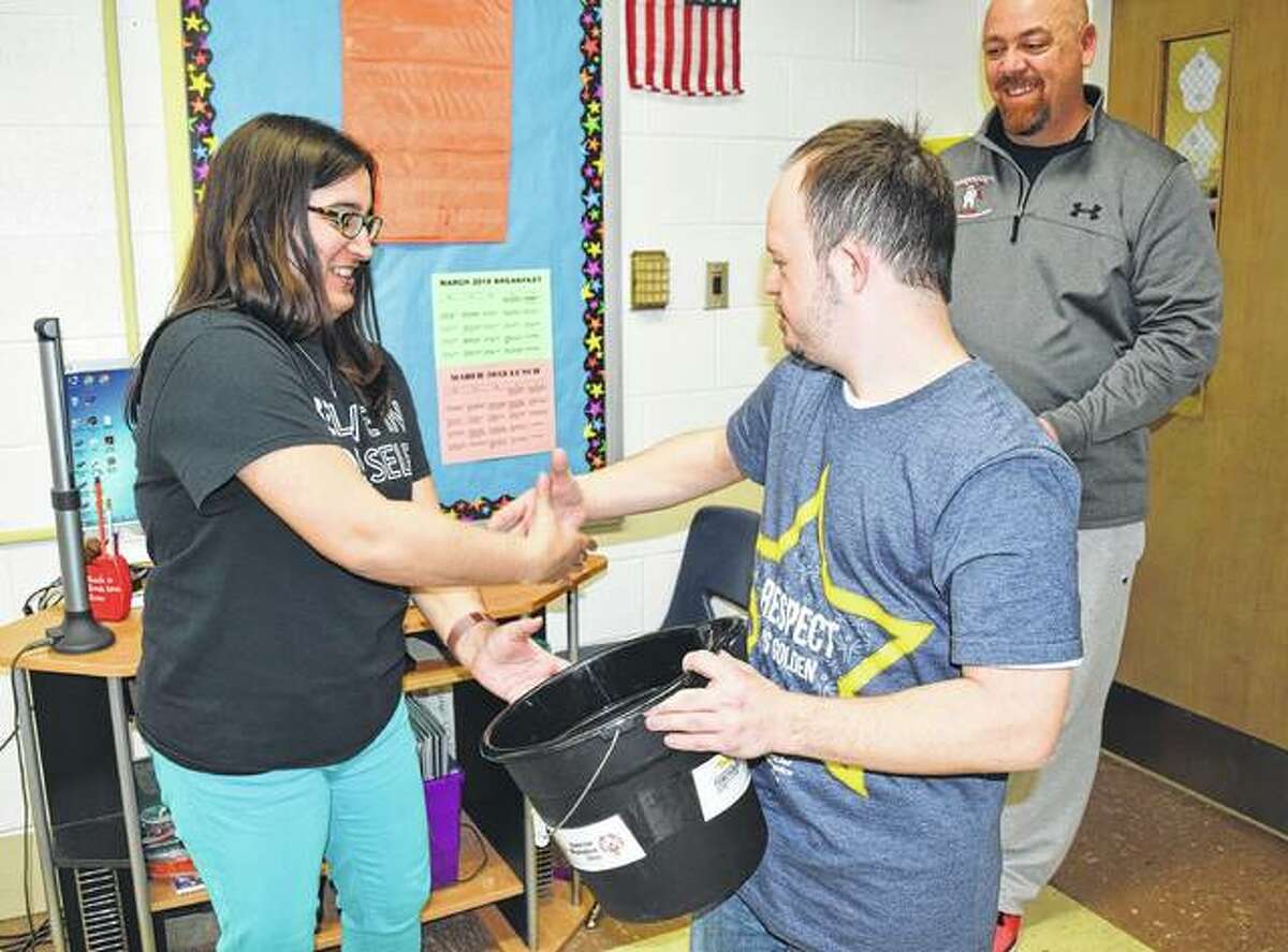 James Foster, a global messenger for Special Olympics, gives a bucket to third grade teacher Raquel Romero Friday to collect pennies during the Meredosia-Chambersburg penny wars to raise money for the Special Olympics.