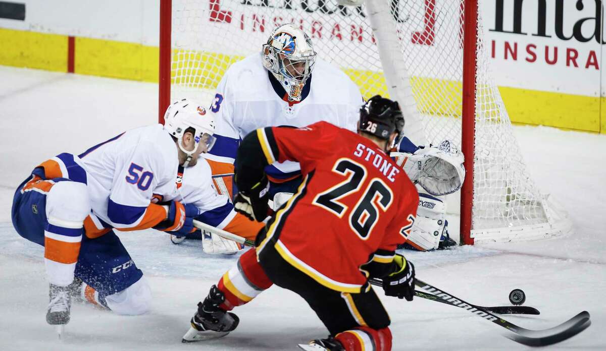 New York Islanders' Adam Pelech, left, helps goalie Christopher Gibson, center, of Finland, by swatting the puck away from Calgary Flames' Michael Stone during second-period NHL hockey game action in Calgary, Alberta, Sunday, March 11, 2018. (Jeff McIntosh/The Canadian Press via AP)