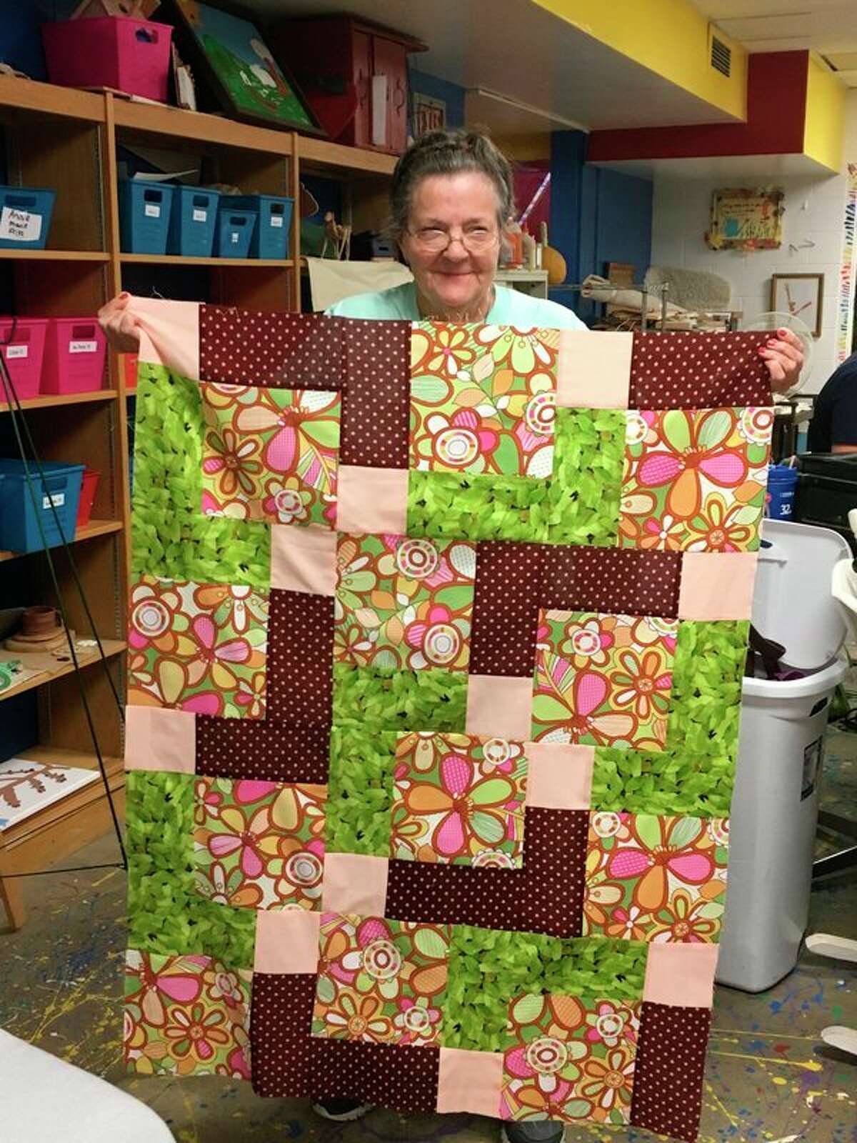 A student in a quilting class at Creative 360 holds up a completed quilt. (Photo provided)