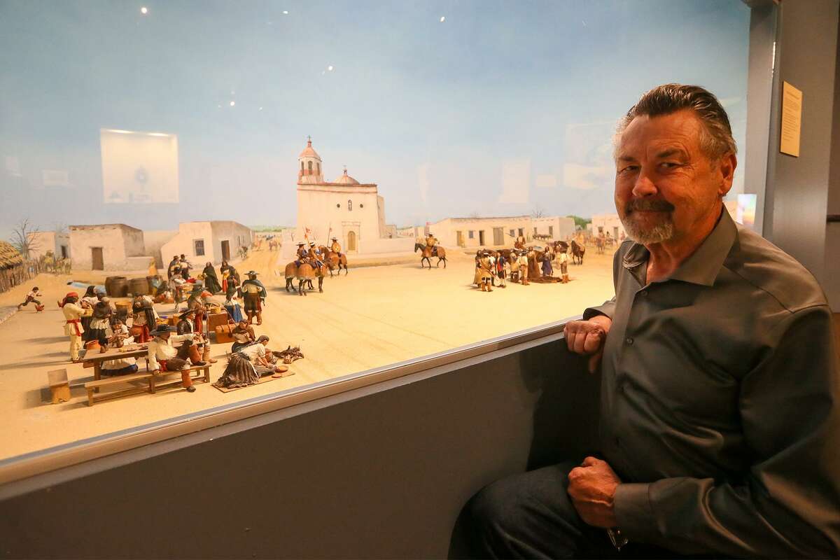 George Nelson kneels beside a model he built, "Plaza de las Islas, Main Plaza 1780," showing a trade day in Main Plaza.