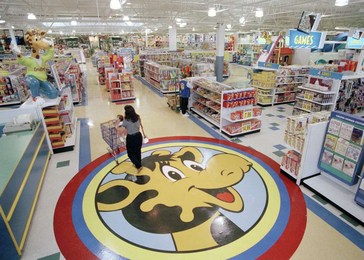 FILE- In this July 30, 1996, file photo, a woman pushes a shopping cart over a graphic of Toys R Us mascot Geoffrey the giraffe at the Toys R Us store in Raritan, N.J. Toys R Us CEO David Brandon told employees Wednesday, March 14, 2018, that the company's plan is to liquidate all of its U.S. stores, according to an audio recording of the meeting obtained by The Associated Press. (AP Photo/Daniel Hulshizer, File)