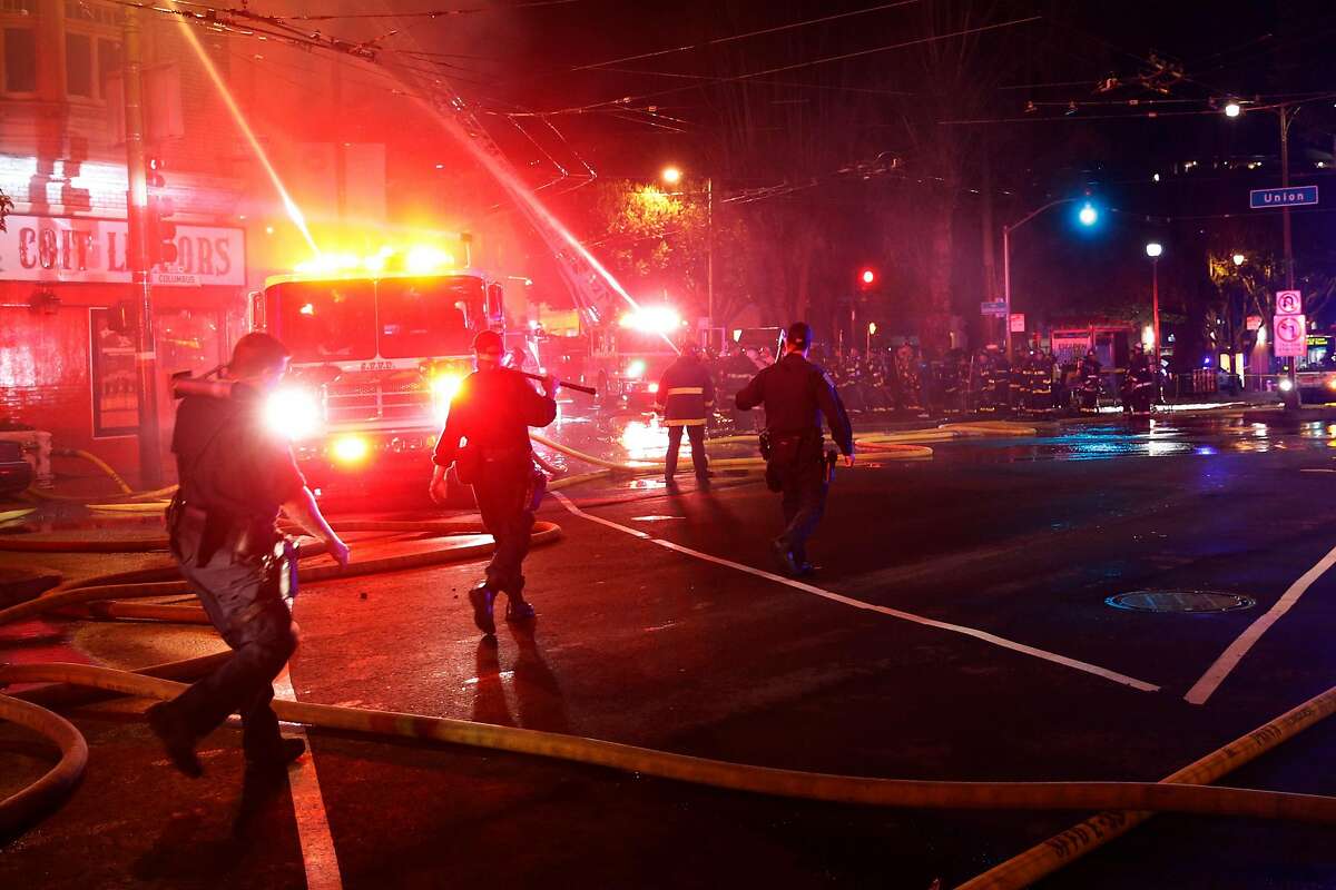 Members of the San Francisco Police Department carry breaching equipment toward the scene of a four-alarm structure fire at the North Beach neighborhood in San Francisco, Calif. on Saturday, March 17, 2018.