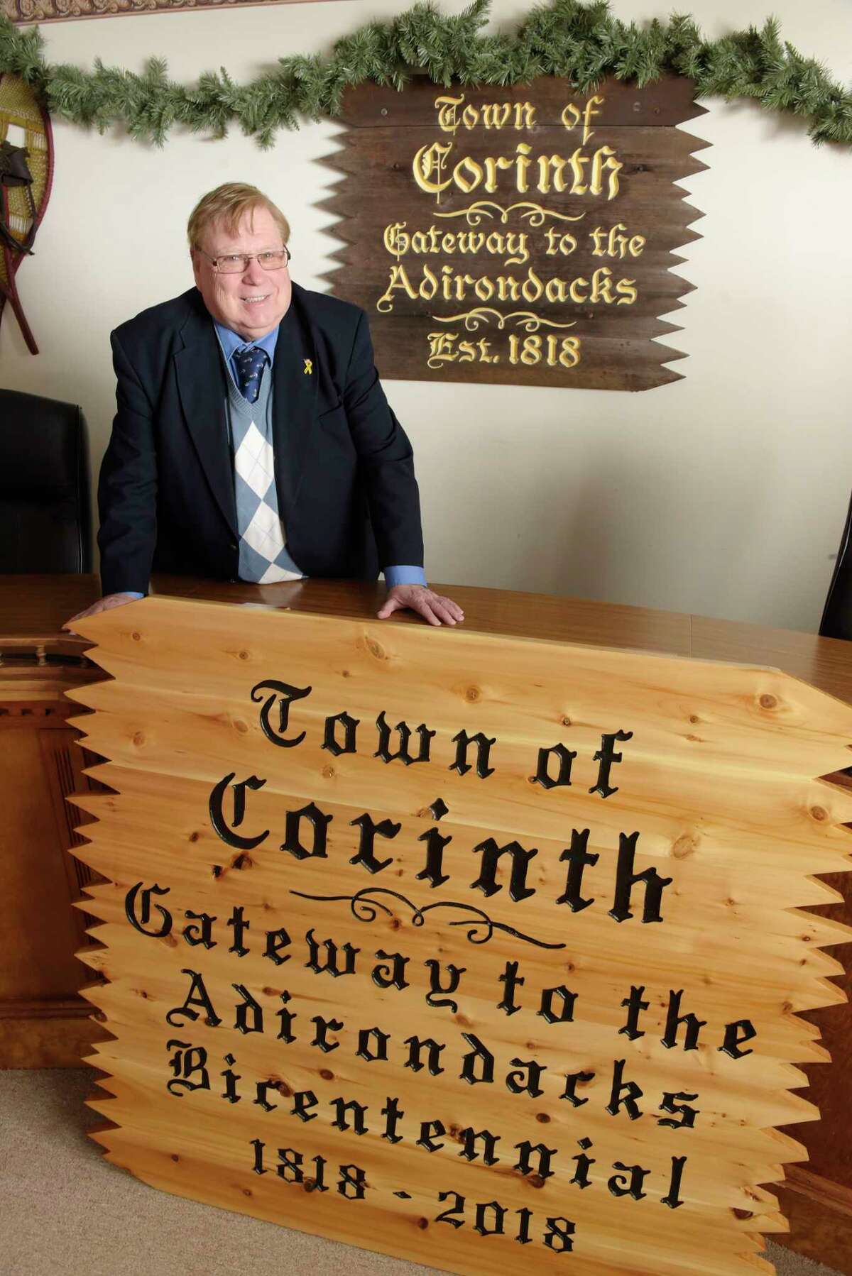 Corinth Town Supervisor Dick Lucia poses with one of the new town signs at Corinth Town Hall on Thursday, March 15, 2018, in Corinth, N.Y. On the wall in the background is the last remaining older town sign. The old sign is over 30 years old, Lucia said. The new signs will be places at the four entrances to the town sometime in the spring. (Paul Buckowski/Times Union)