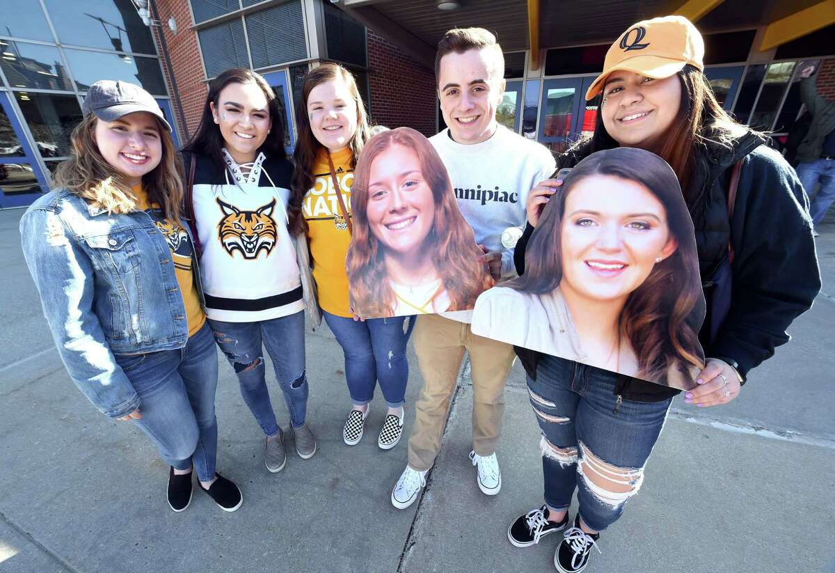 From left, Quinnipiac freshmen Brynn Martin, Caroline King, Katrina Manzari, Jonathan Sweeney and Camila Maturane are photographed in front of the TD Bank Sports Center before boarding a bus headed to Gampel Pavilion on Monday. They are holding photographs of their friends, Quinnipiac players Chiara Bacchini, left, and Danelle Bradley.