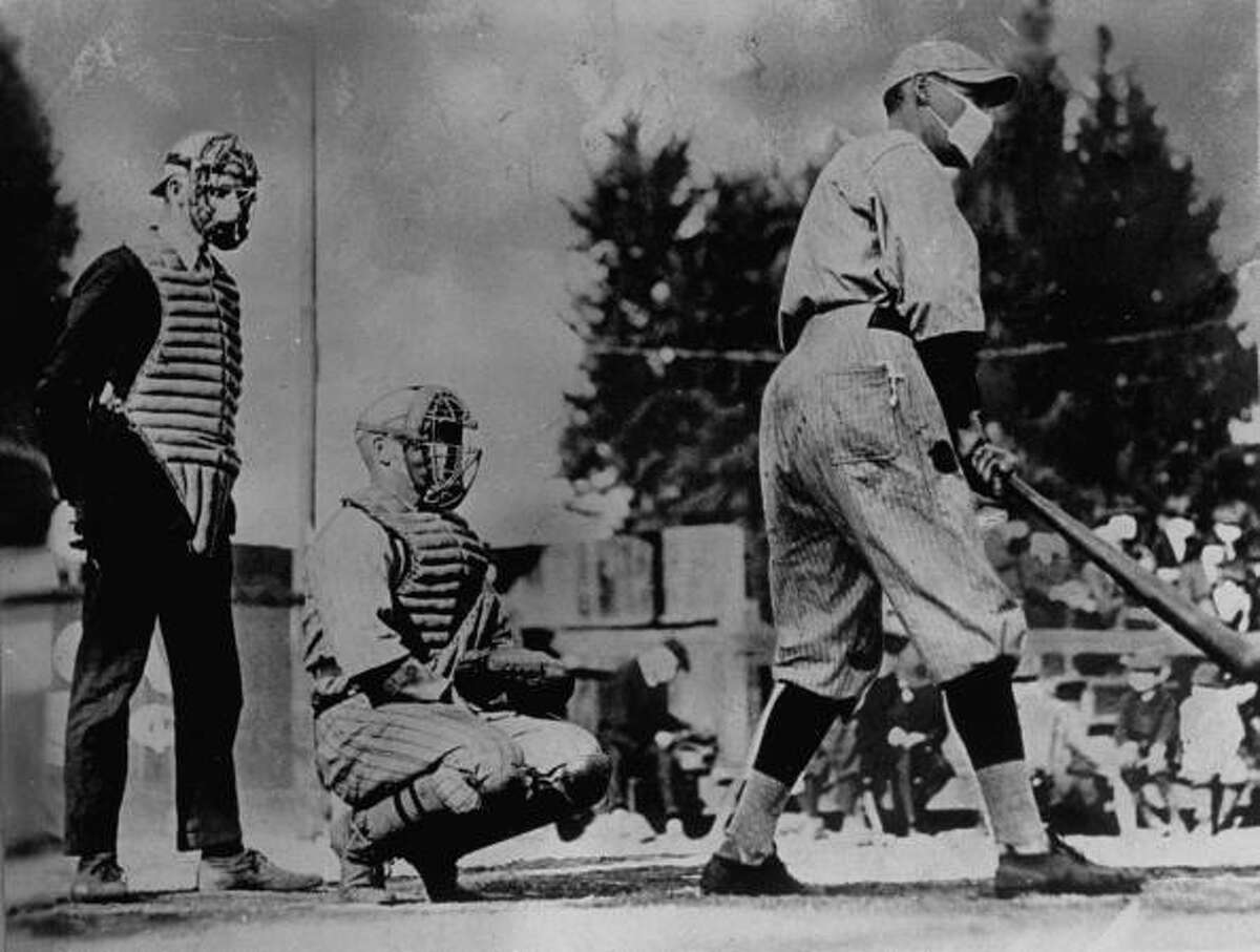 baseball players, one batting & one catching, with umpire standing behind plate, wearing masks which they thought would keep them from getting flu during influenza epidemic of 1918.