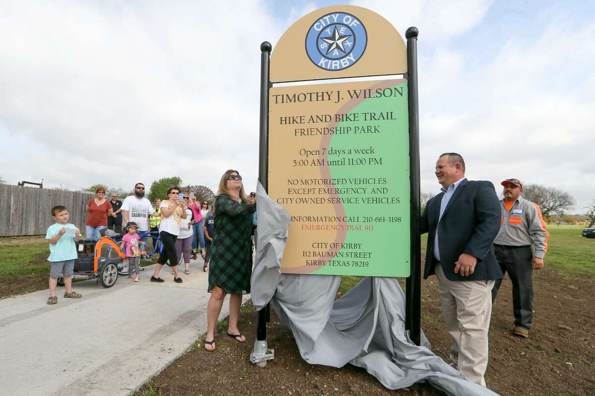 Former Kirby Mayor Tim Wilson (front right) and his wife, Kelly Wilson, unveil the sign at the entrance to the Timothy J. Wilson Hike & Bike Trail at Friendship Park in Kirby during the grand opening/ribbon cutting of the trail on Friday, March 16, 2018. The new trail runs north through Friendship Park for .92 miles from Binz-Engelman Rd to Hugo Lentz Park.