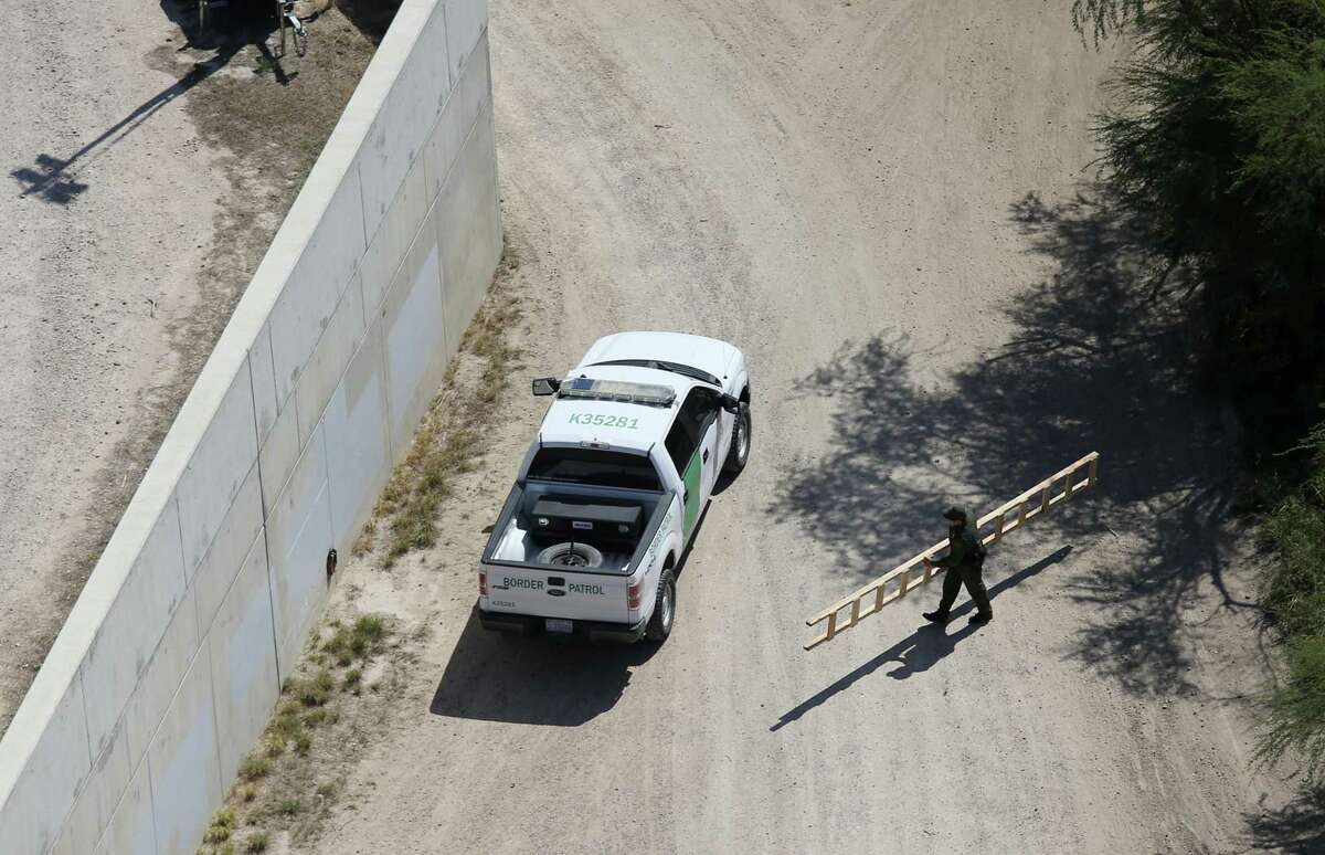 A U.S. Border Patrol agent picks up a ladder hidden in the field by the U.S. Mexico border wall, left, near the McAllen-Hidalgo International Bridge, Tuesday, Oct. 4, 2016. A unit with the U.S. Customs and Border Protection Air and Marine Operations flying a Bell Huey helicopter spotted the ladder. Smugglers use ladders to crossing immigrants and drugs over the wall.