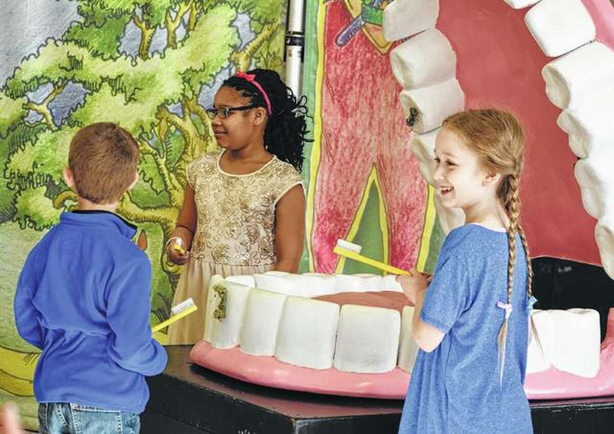 Murrayville-Woodson first-grader Kole Law (from left), third-grader Jaryah Thompson and second-grader Marley Coultas prepare Thursday to brush plaque from the teeth of a giant mouth during a program at the school.