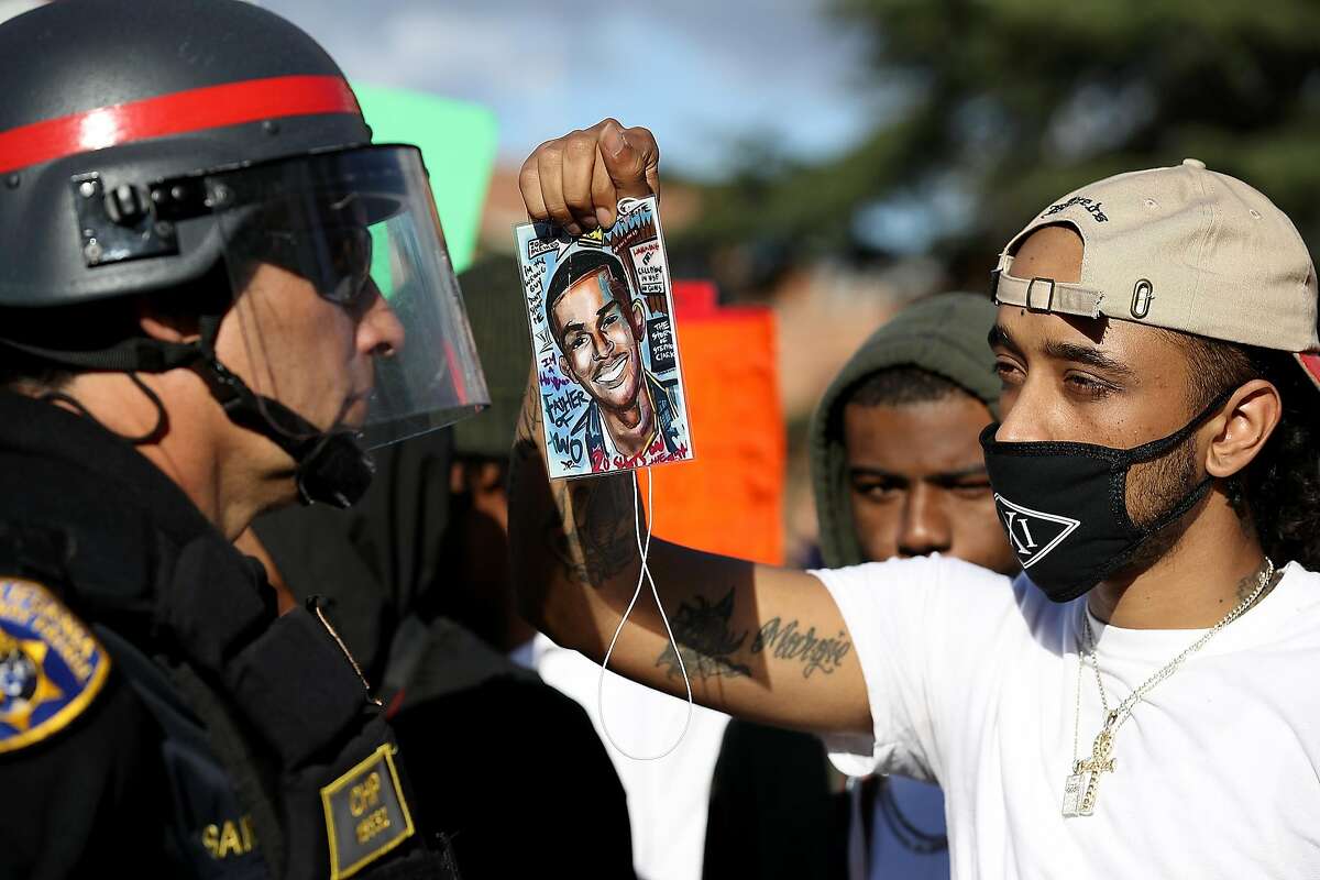 A Black Lives Matter protester holds a photo of Stephon Clark in front of a California Highway Patrol officer as they block an entrance to Interstate 5 during a demonstration on March 23, 2018 in Sacramento. 