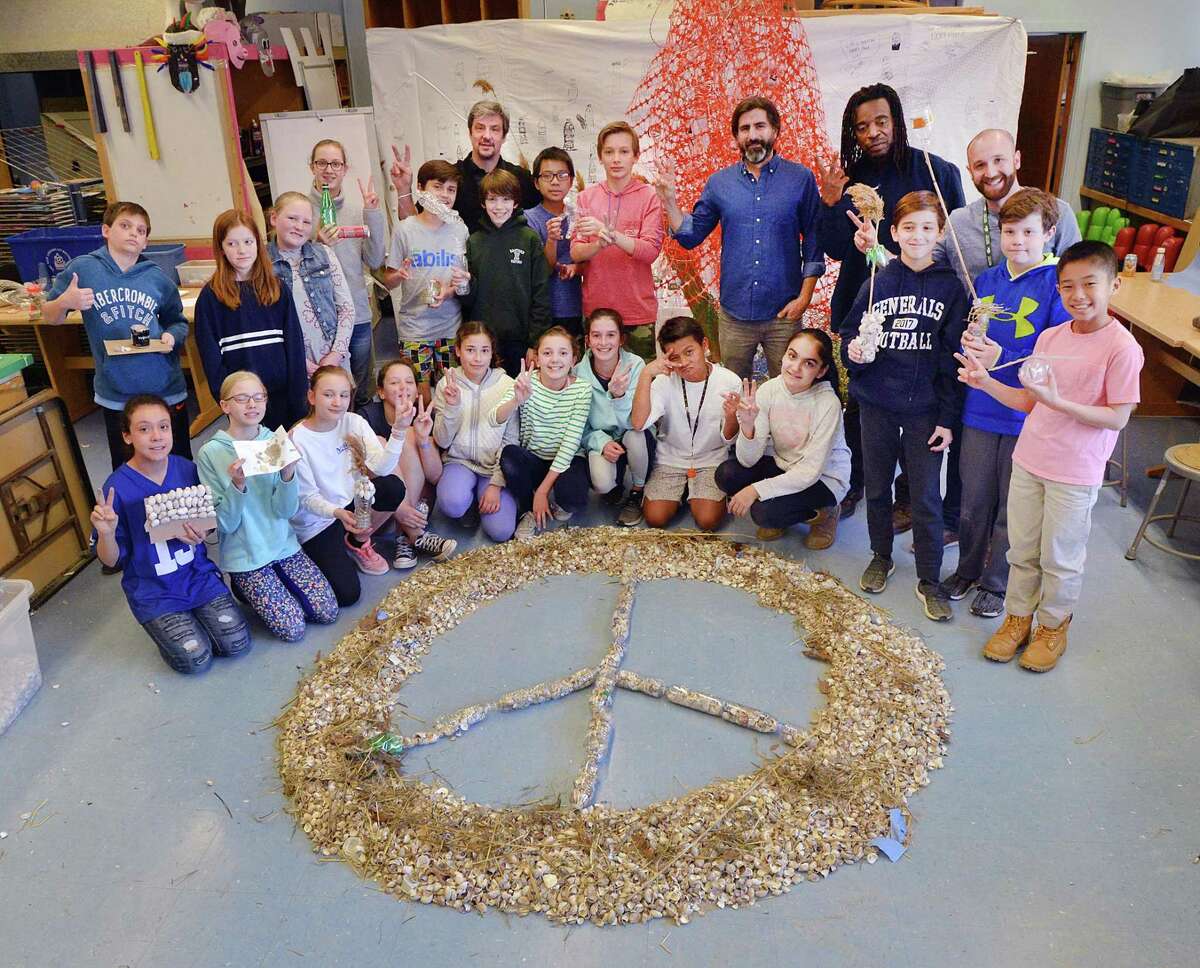 Posing for a photo, Eastern Middle School sixth grade students with the help of visiting environmental artists, Willie Cole and Alejandro Duran, created a peace sign made of seashells, plastic pollution and discarded items collected from Tod's Point as part of their "Message in a Bottle" art project dealing with pollution, done during class at the school in Greenwich, Conn., Friday, March 23, 2018.