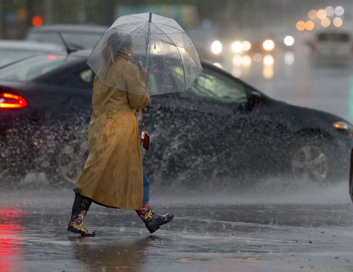 A woman walks with an umbrella through the intersection of Hildebrand Avenue and Broadway as cars splash by during a rainstorm that swept through San Antonio.