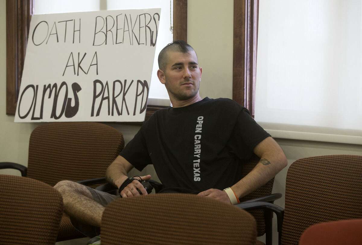 David Nunez sits with a sign Thursday at Olmos Park City Hall while the Olmos Park City Council meets in executive session to discuss an ordinance prohibiting people other than police from carrying long guns in public, a conflict with state law. The council repealed the ordinance.