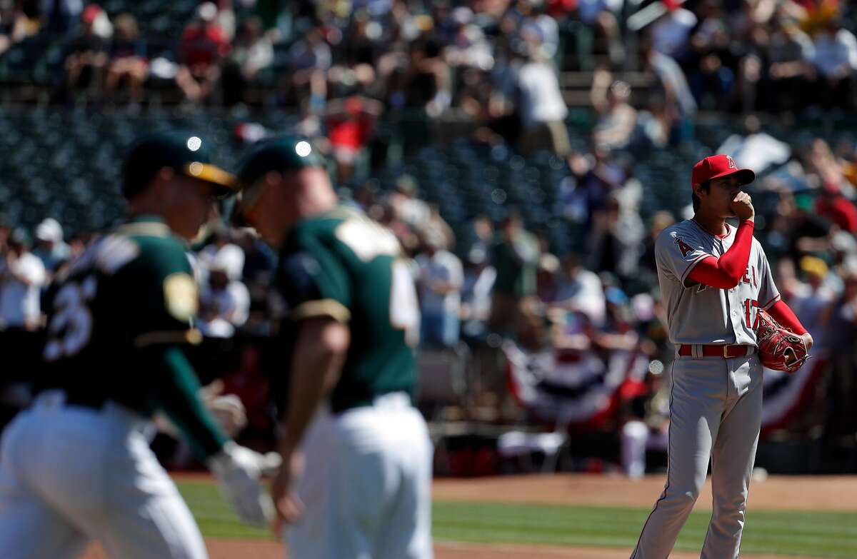 Shohei Ohtani (17) stands on the mound as third base coach Matt Williams high fives Matt Chapman (26) after Chapman hit a three-run homerun in the second inning as the Oakland Athletics played the Los Angeles Angels of Anaheim at the Oakland Coliseum in Oakland on Sunday, April 1, 2018.